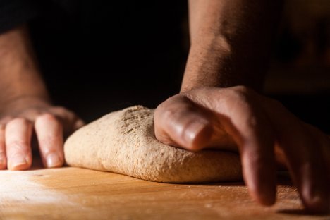 Das Bild zeigt zwei Hände, die auf einer bemehlten Fläche einen Brotteig kneten.