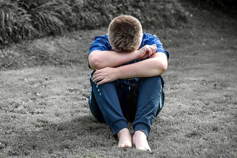 Das Foto zeigt einen Jungen, der traurig seinen Kopf in Arme und Schoß vergräbt.