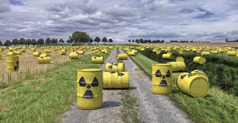 Das Foto zeigt gelbe Fässer mit einem Warnzeichen für atomare Strahlung, die auf einem Feld vrerteilt sind. 